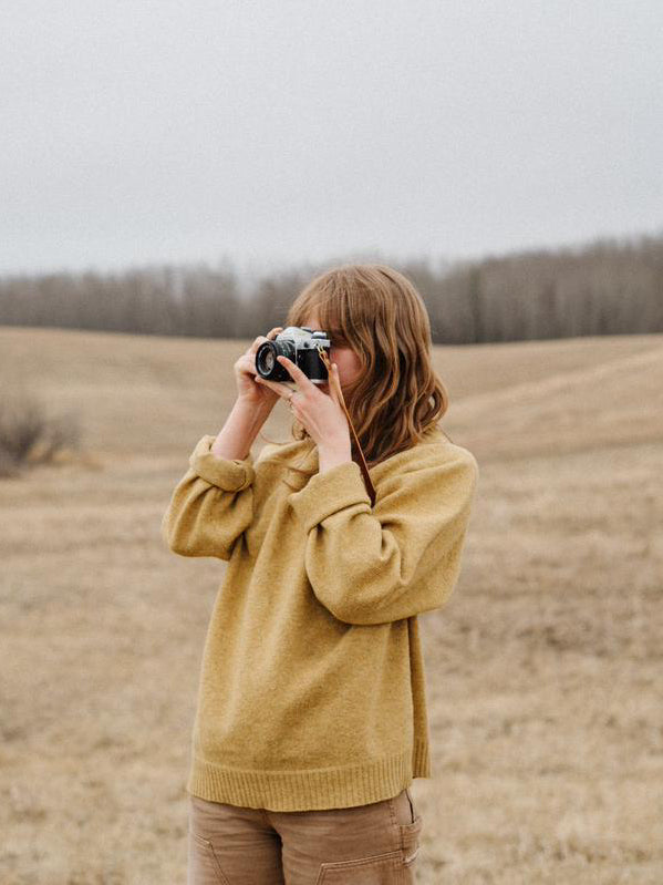 girl in a field taking pictures using her handmade leather camera strap